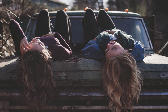 girls laying on a car bonnet